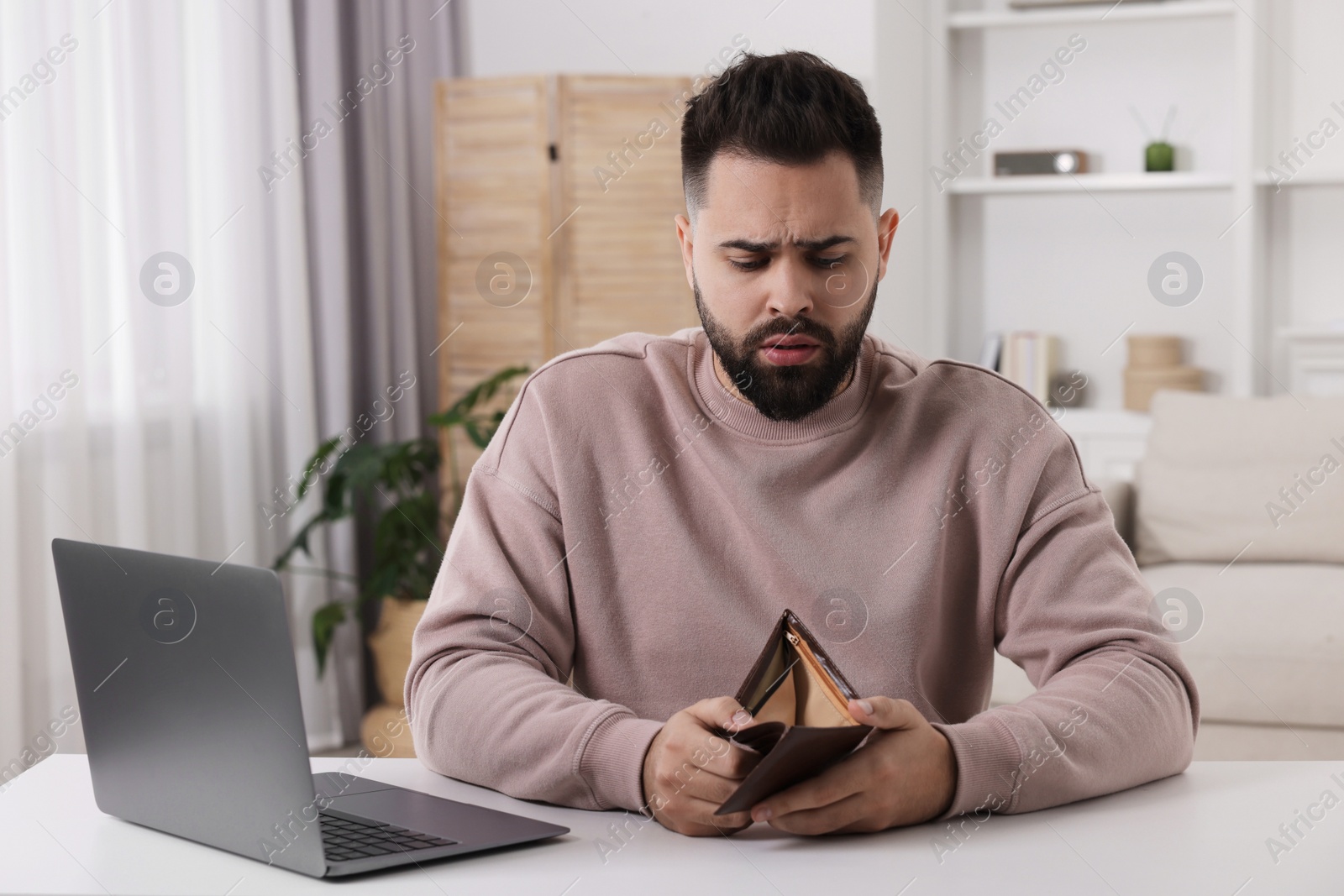 Photo of Upset man with empty wallet at white table indoors