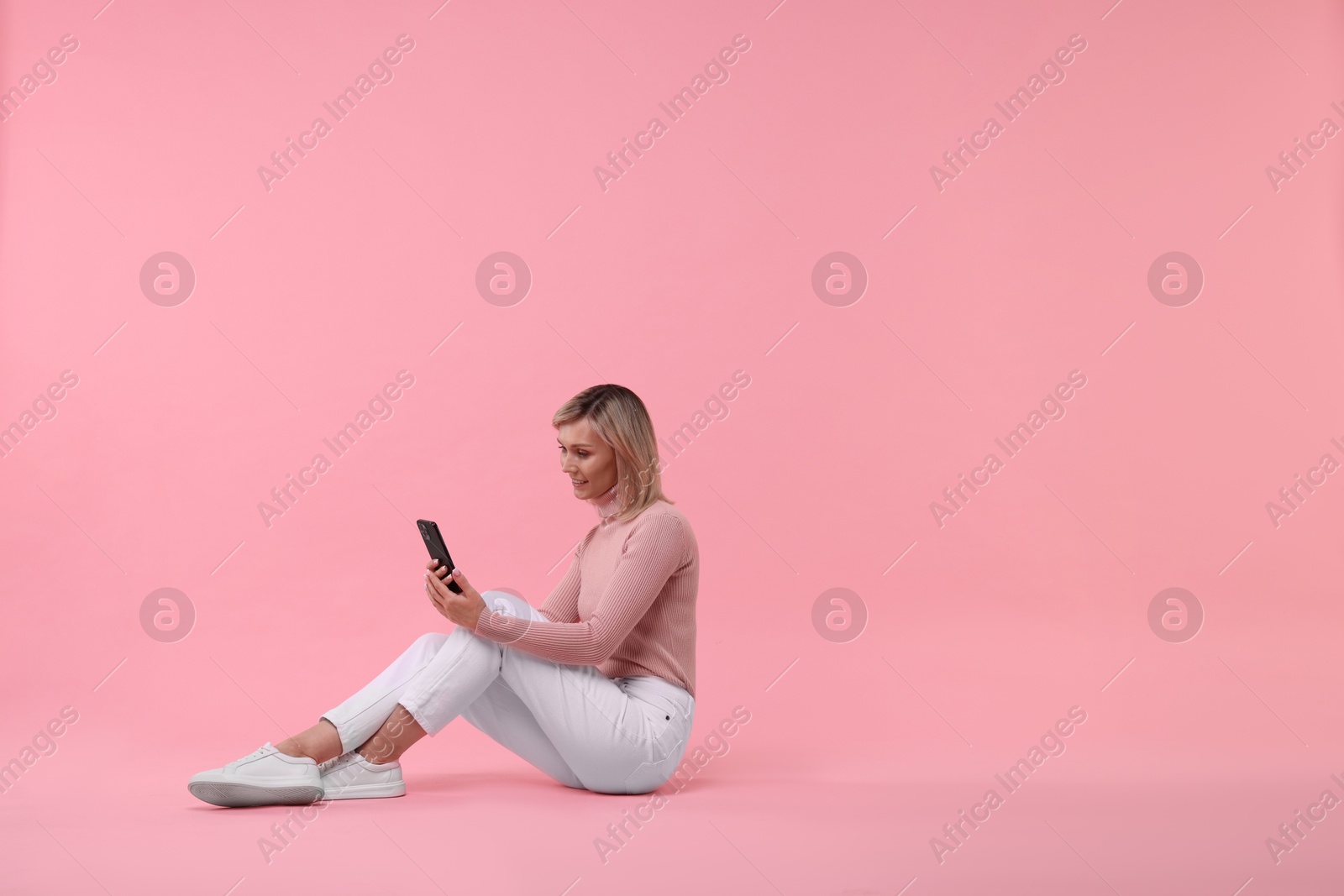 Photo of Happy woman with phone on pink background, space for text