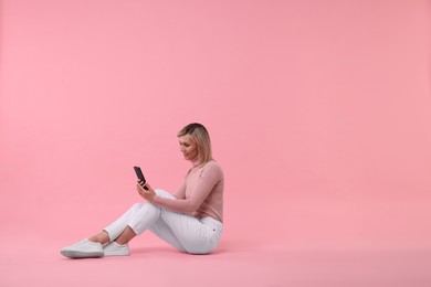 Happy woman with phone on pink background, space for text