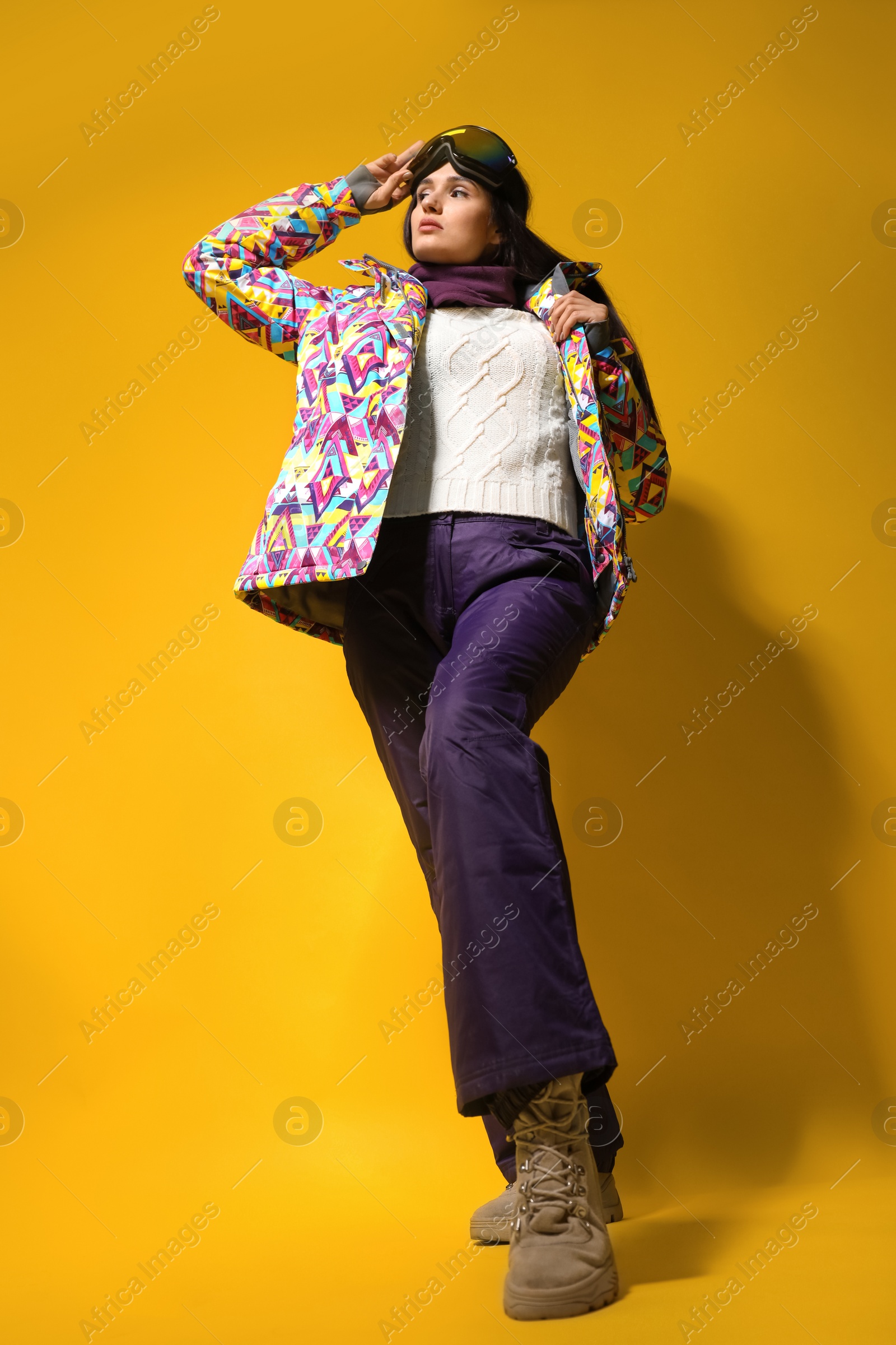 Photo of Woman wearing stylish winter sport clothes on yellow background, low angle view