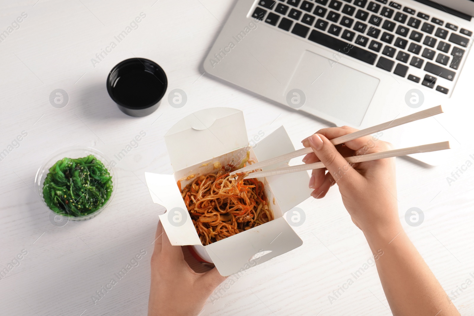 Photo of Woman eating tasty Chinese noodles at workplace, closeup. Food delivery