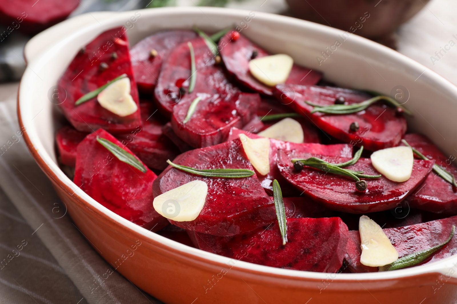 Photo of Baking dish with raw beetroot slices, garlic and rosemary on table, closeup