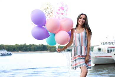 Photo of Pretty young woman with color balloons near river