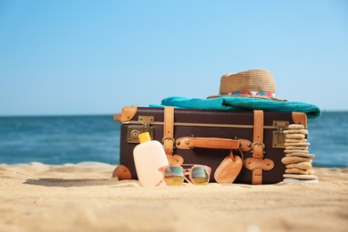 Photo of Suitcase and beach accessories on sand near sea. Space for text