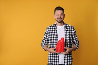 Photo of Man holding red container of motor oil on orange background. Space for text