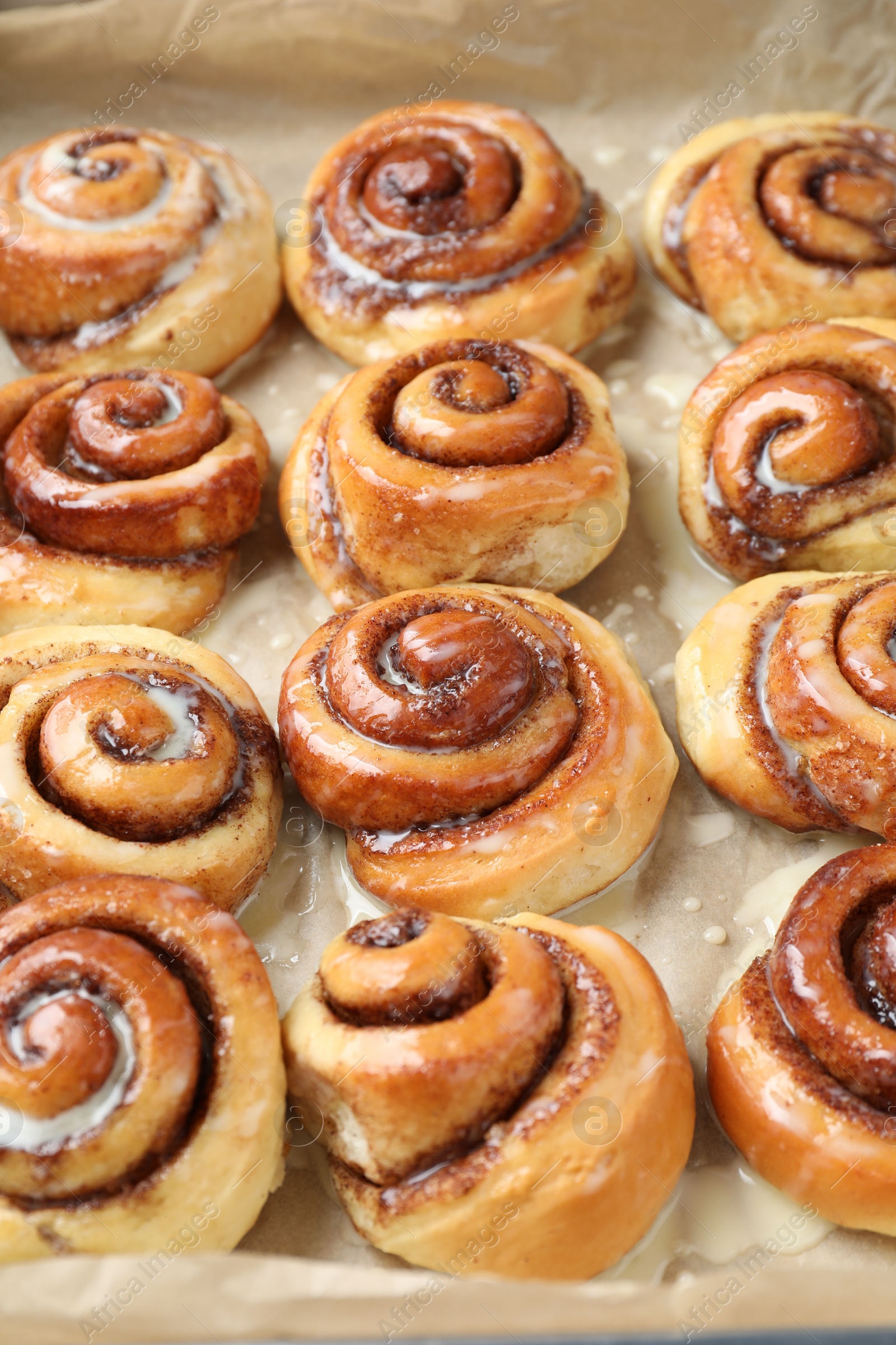 Photo of Tasty cinnamon rolls with cream on parchment paper