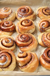 Photo of Tasty cinnamon rolls with cream on parchment paper