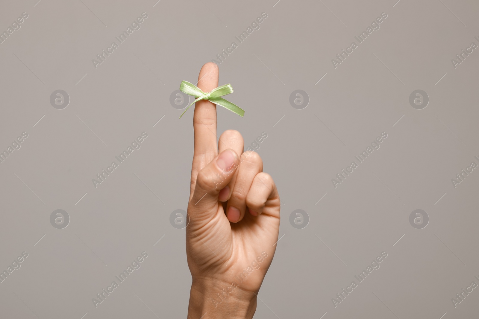 Photo of Woman showing index finger with tied bow as reminder on grey background, closeup