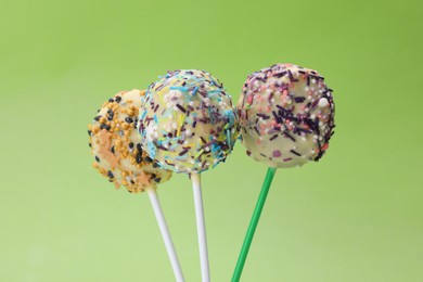 Photo of Sweet cake pops decorated with sprinkles on light green background, closeup. Delicious confectionery
