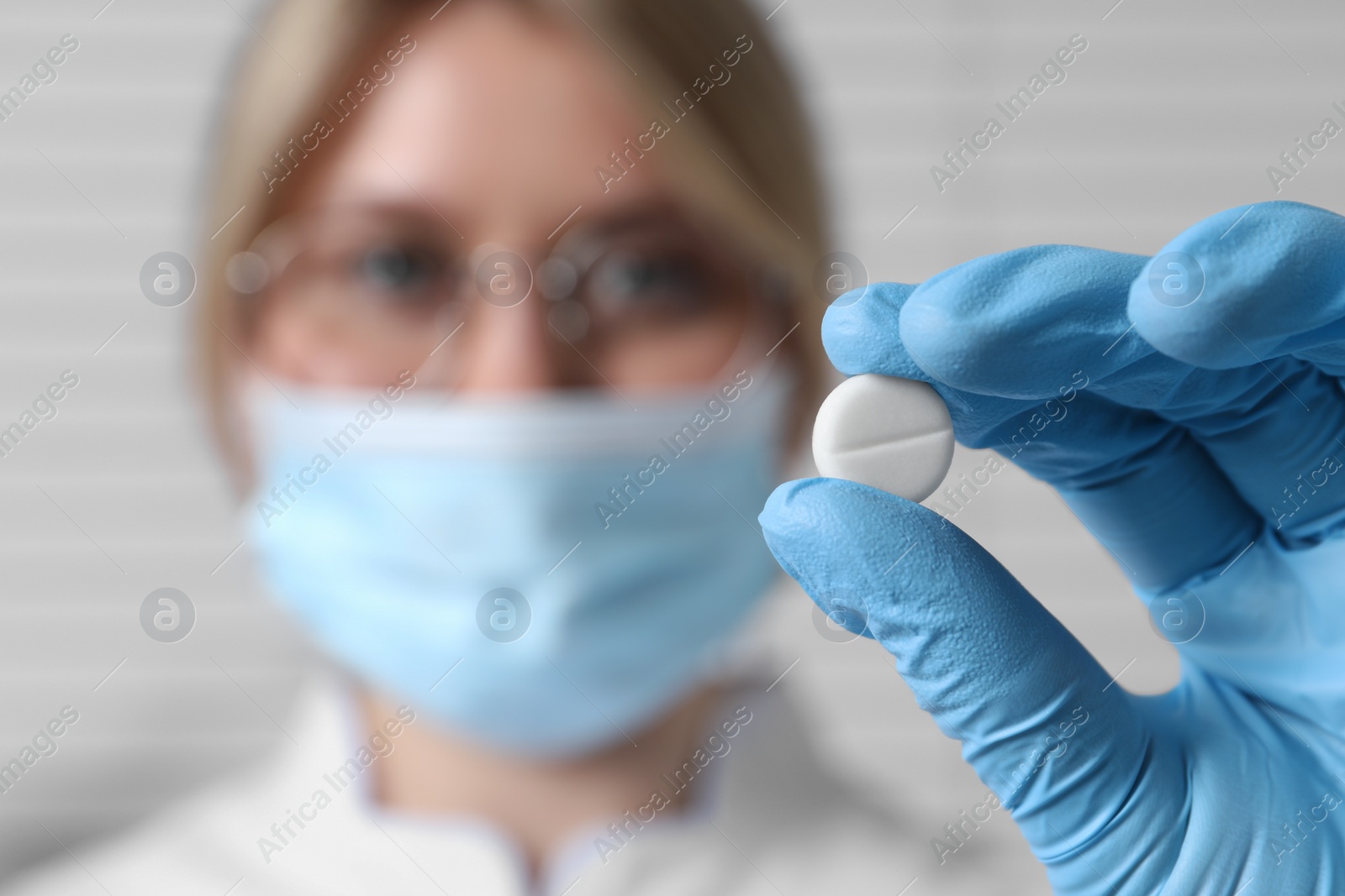 Photo of Doctor holding pill on light background, selective focus. Space for text