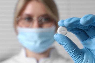 Photo of Doctor holding pill on light background, selective focus. Space for text