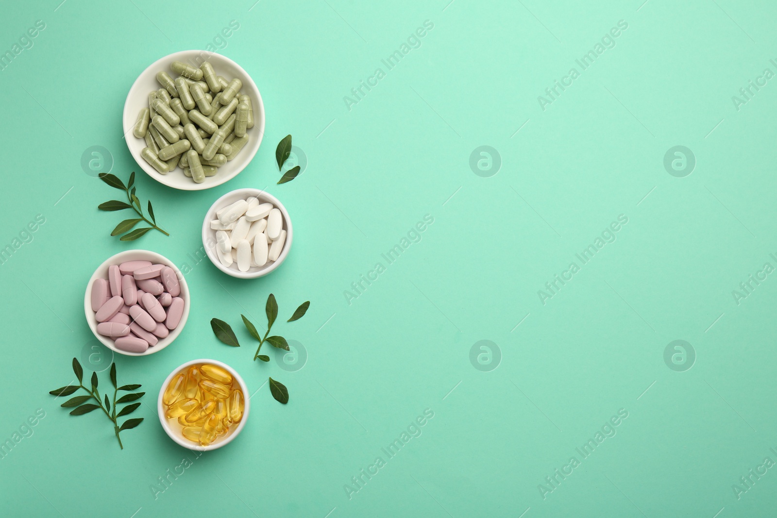 Photo of Different vitamin capsules in bowls and leaves on turquoise background, flat lay. Space for text