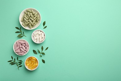 Photo of Different vitamin capsules in bowls and leaves on turquoise background, flat lay. Space for text