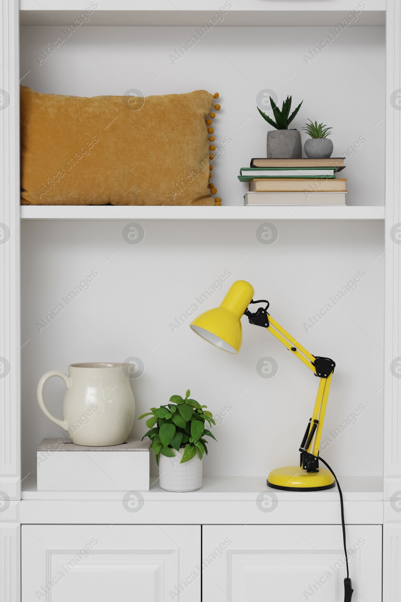 Photo of Shelves with lamp, books and different decor indoors. Interior design