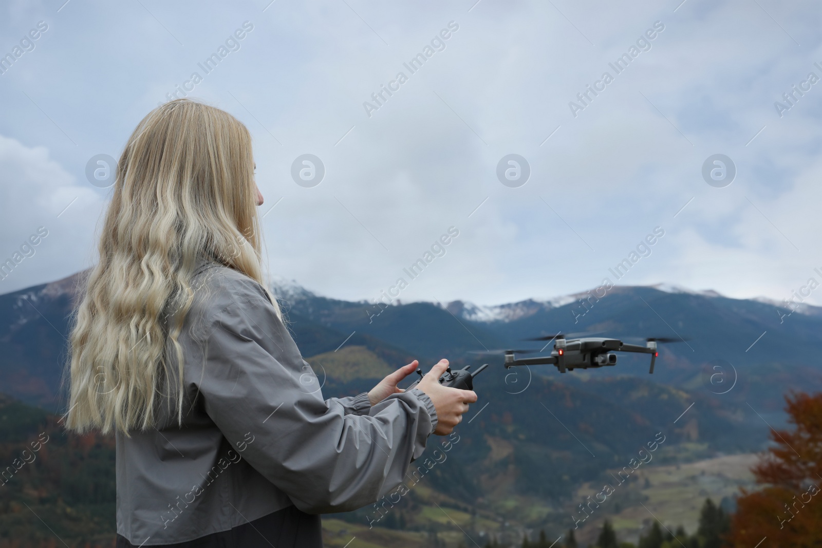 Photo of Young woman operating modern drone with remote control in mountains