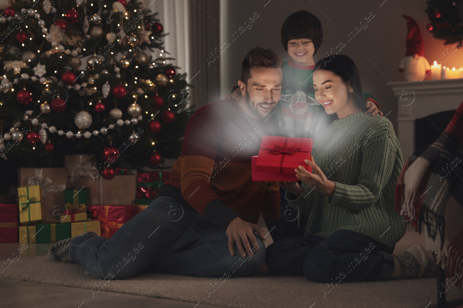 Image of Happy family opening gift box with magical light at home. Christmas celebration