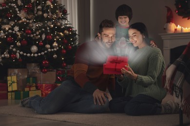 Image of Happy family opening gift box with magical light at home. Christmas celebration