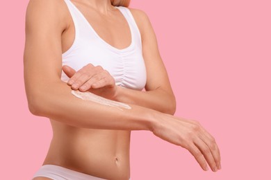 Photo of Woman applying body cream onto her arm against pink background, closeup