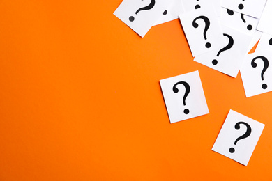 Photo of Paper notes with question marks on orange background, flat lay. Space for text