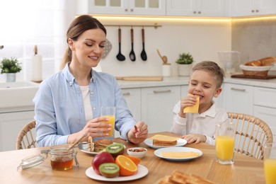 Photo of Mother and her cute little son having breakfast at table in kitchen