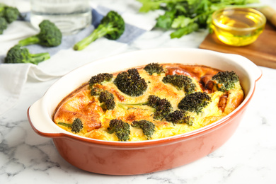 Photo of Tasty broccoli casserole in baking dish on white marble table