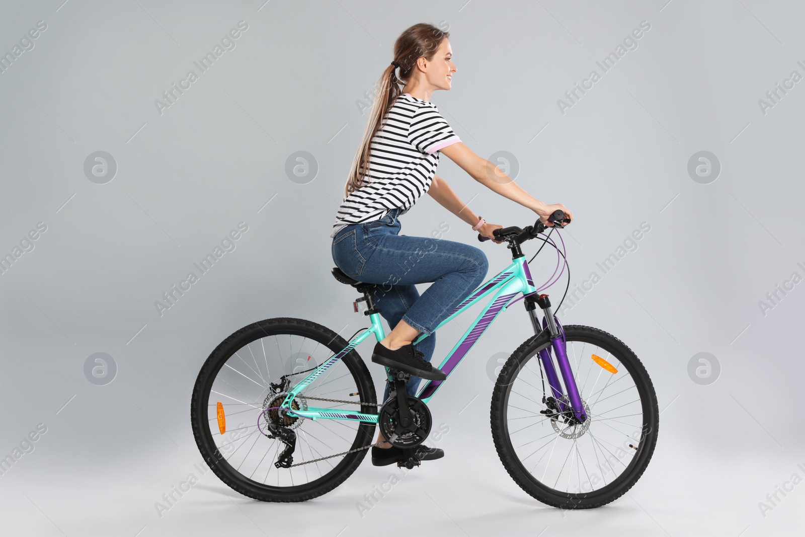 Photo of Happy young woman riding bicycle on grey background