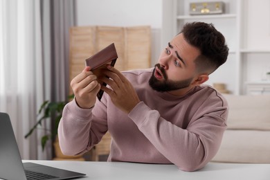 Photo of Confused man with empty wallet at white table indoors