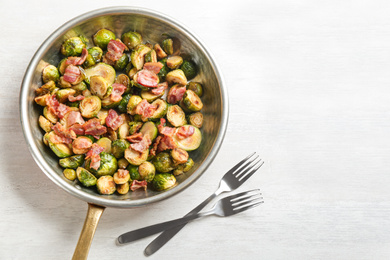 Roasted Brussels sprouts with bacon on white wooden table, flat lay. Space for text