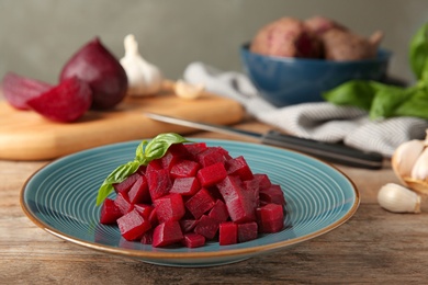 Photo of Plate of cut boiled beets with basil on wooden table