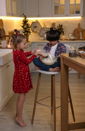 Photo of Cute little children making dough for Christmas cookies in kitchen