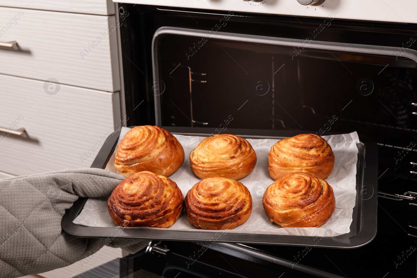 Photo of Woman taking freshly baked buns out of oven, closeup