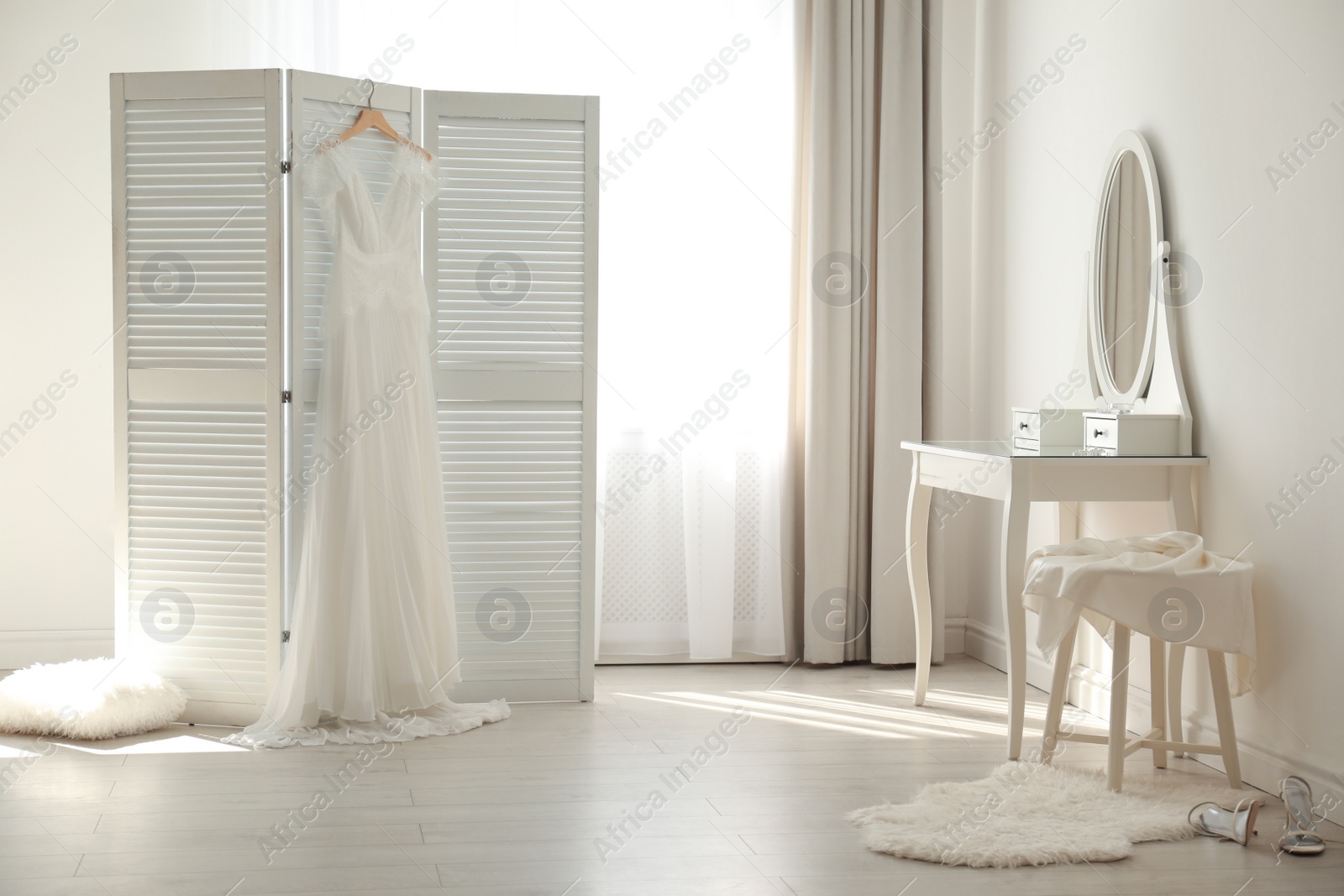 Photo of Beautiful wedding dress hanging on folding screen in room