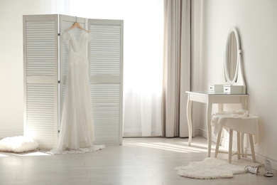 Beautiful wedding dress hanging on folding screen in room