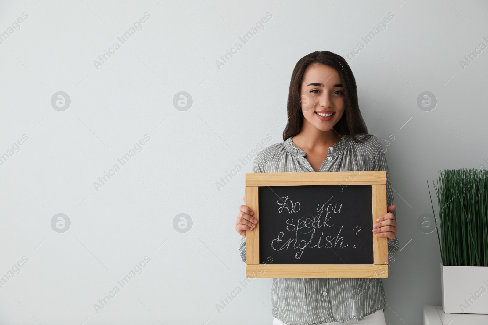 Photo of Young female teacher holding chalkboard with words DO YOU SPEAK ENGLISH? on light background. Space for text