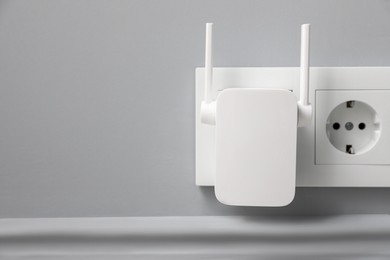 Wireless Wi-Fi repeater on light grey wall, space for text