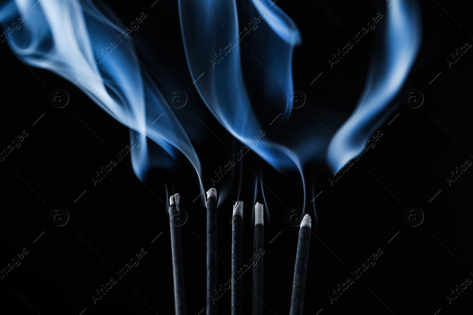 Photo of Incense sticks smoldering on black background, closeup