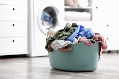 Photo of Plastic basket with dirty laundry on floor indoors, space for text