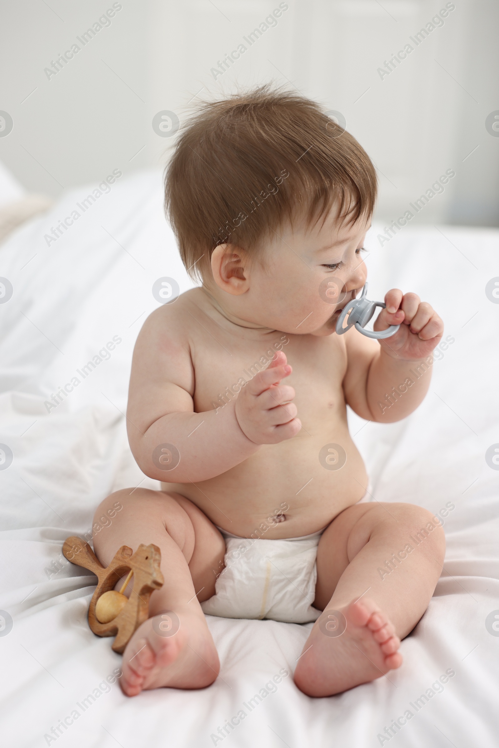 Photo of Cute baby boy with pacifier and wooden rattle on bed at home