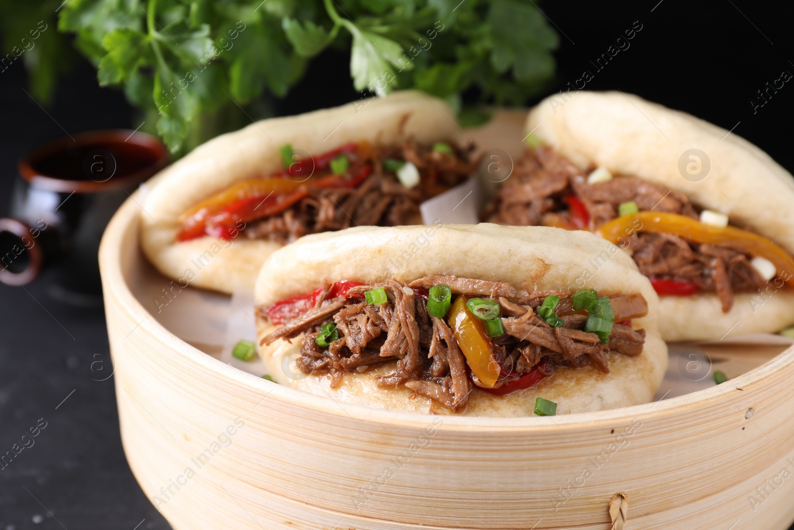 Photo of Delicious gua bao in bamboo steamer on black table, closeup