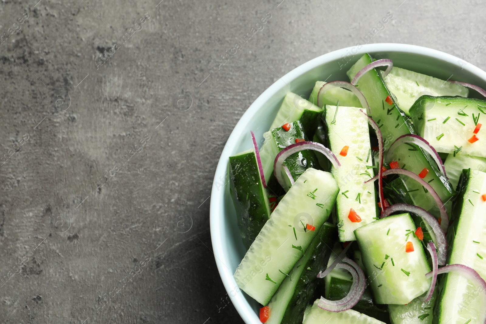 Photo of Delicious cucumber salad with onion in bowl on grey background, top view. Space for text