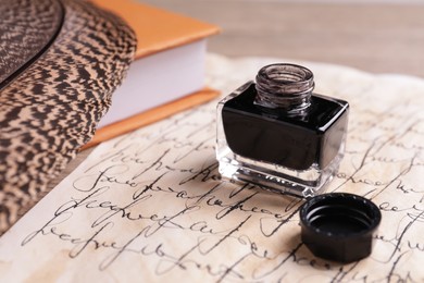 Photo of Open inkwell, feather, book and vintage parchment with text on table, closeup