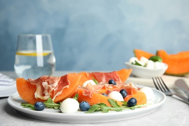 Photo of Fresh melon with prosciutto, mozzarella and arugula on table