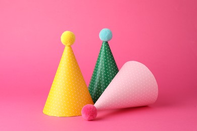 Photo of Beautiful party hats with pompoms on pink background