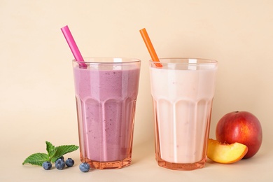 Tasty blueberry and peach milk shakes in glasses on beige background