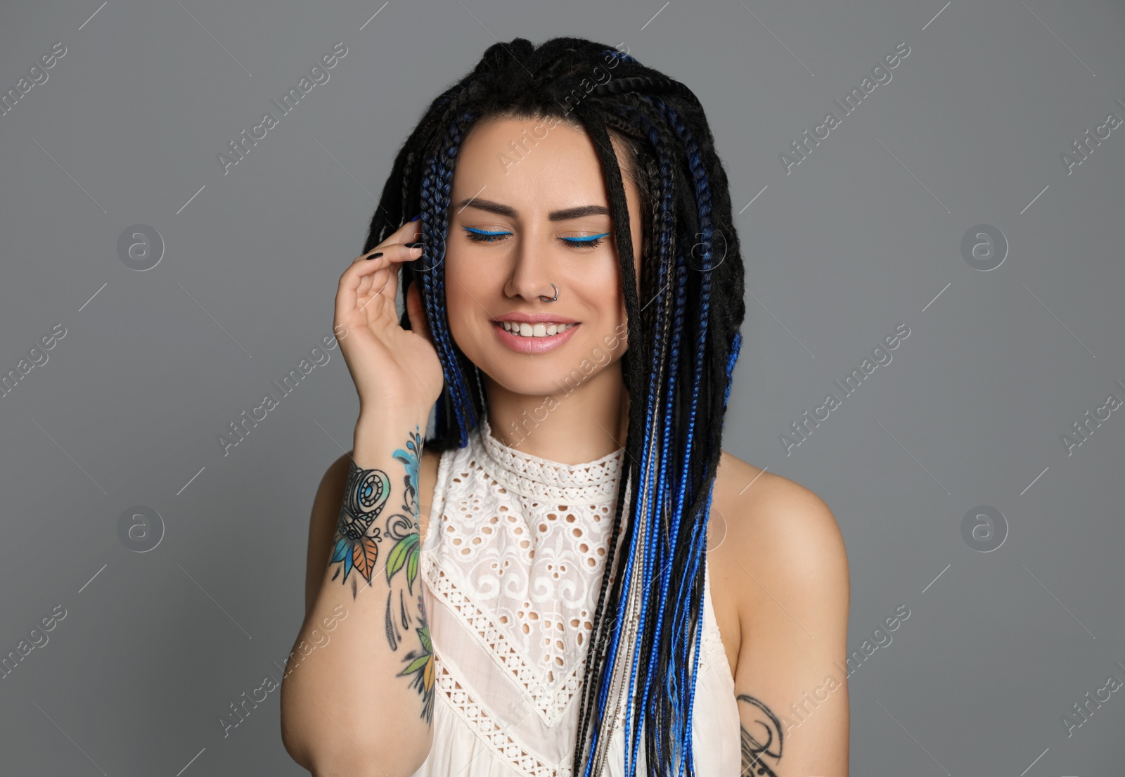 Photo of Beautiful young woman with nose piercing and dreadlocks on grey background