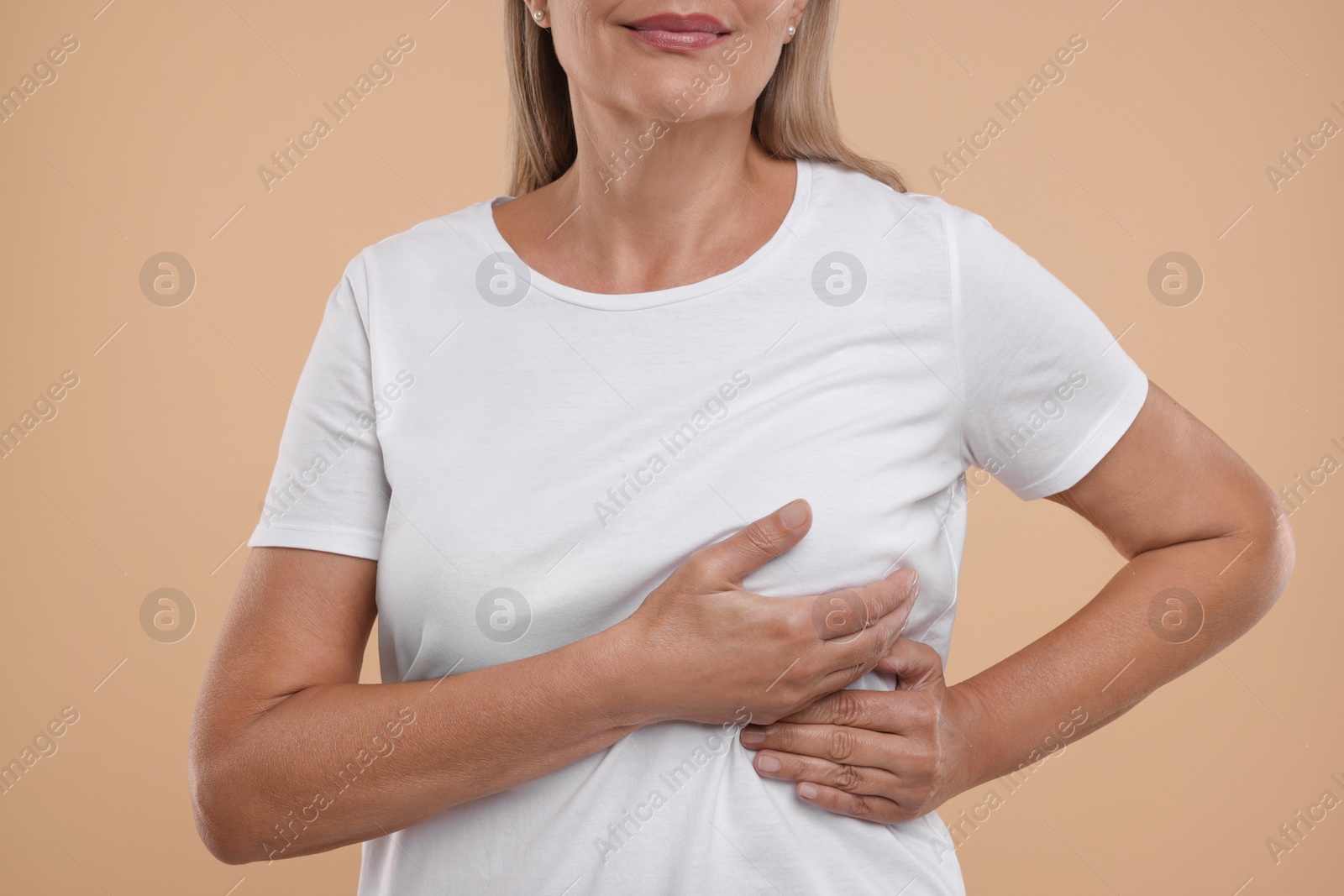 Photo of Woman doing breast self-examination on light brown background, closeup