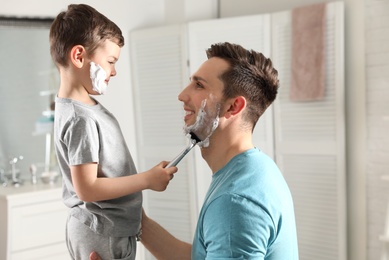 Photo of Little son shaving his dad in bathroom