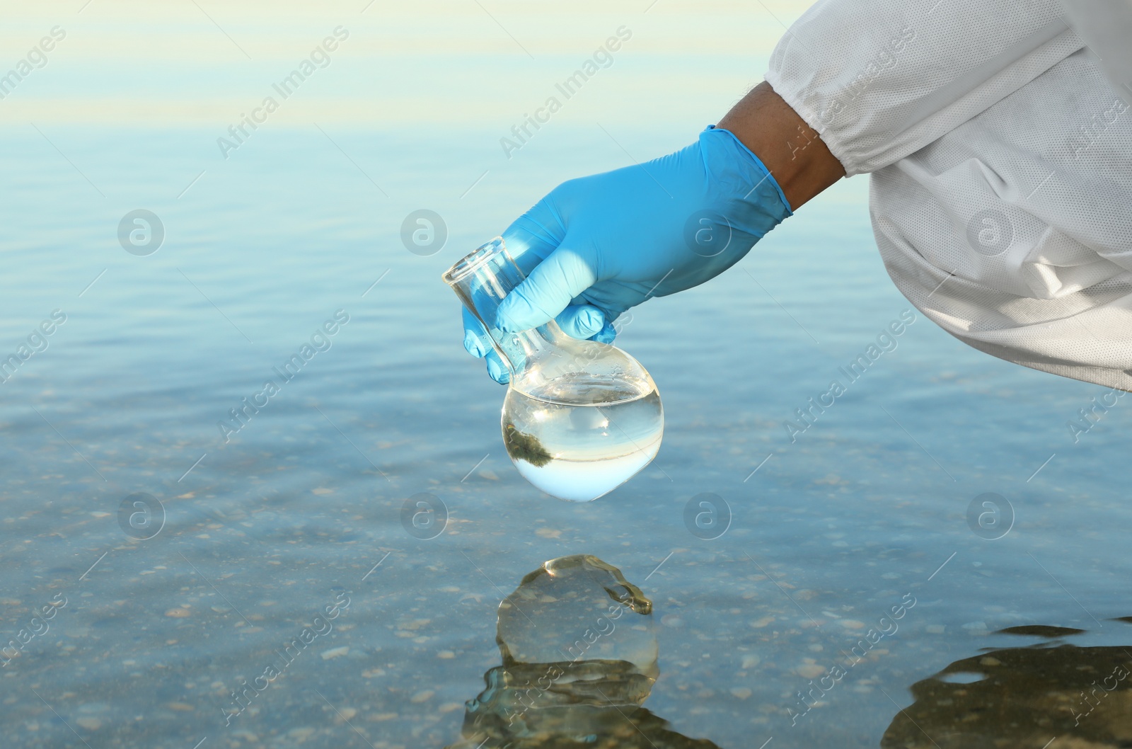 Photo of Scientist with florence flask taking sample from river for analysis, closeup