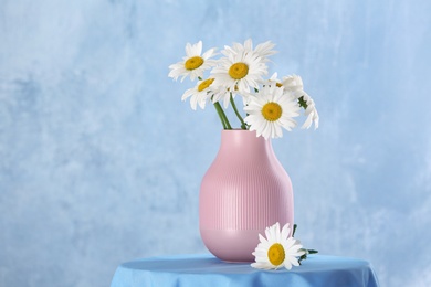 Beautiful tender chamomile flowers in vase on table against color background, space for text