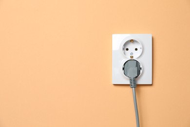 Photo of Double power socket with inserted plug on pale orange wall, space for text. Electrical supply